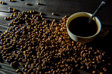 a cup of coffee stands on a black wooden table, coffee beans are scattered around.