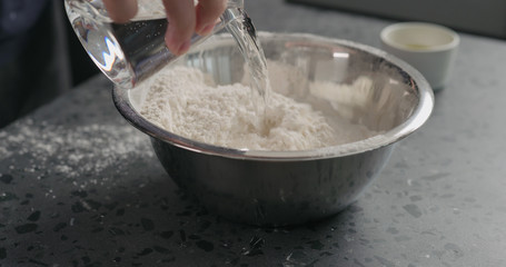 man adds wet ingredients into flour in steel bowl on concrete countertop