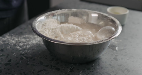 wet ingredients into flour in steel bowl on concrete countertop