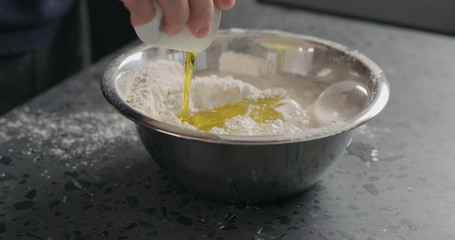 man adds wet ingredients into flour in steel bowl on concrete countertop