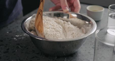 man mixing dry ingredients with flour in steel bowl on concrete countertop