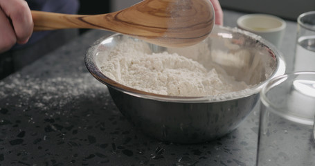 man mixing dry ingredients with flour in steel bowl on concrete countertop