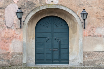 Fototapeta na wymiar green arched wooden door and lanterns on the sides, Italy