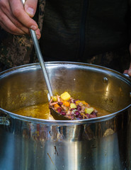 soup pot, with a large spoon distributed soup, cooked in nature on the fire; focus and sharpness in certain places