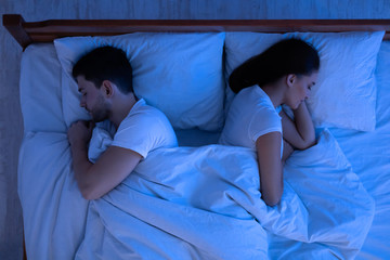 Fototapeta na wymiar Spouses Sleeping Lying Back-To-Back In Bed In Bedroom, Above View