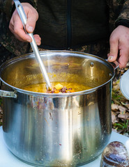 soup pot, with a large spoon distributed soup, cooked in nature on the fire; focus and sharpness in certain places