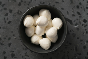 top view of small mozzarella balls in black bowl on concrete background