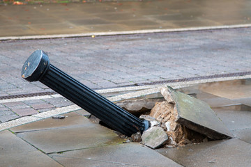 Damaged black bollard knocked down in busy street