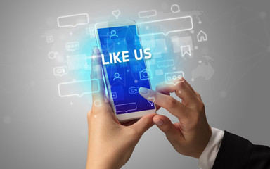 Female hand typing on smartphone with LIKE US inscription, social media concept