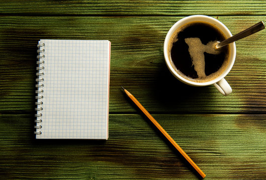 pencil padand and a cup of coffee on a green wooden table.