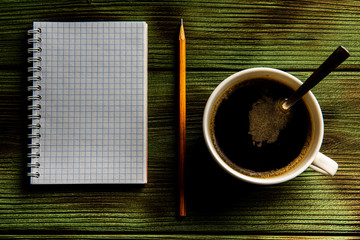 pencil padand and a cup of coffee on a green wooden table.