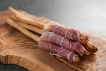 Grissini with prosciutto on olive wood board