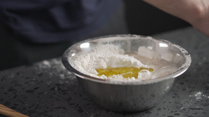 man adds wet ingredients into flour in steel bowl on concrete countertop