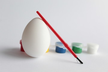 White egg on a white background. Nearby are the brush and paint. Easter concept. There is a place for text.