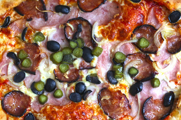 pizza texture background with hum, sausage,cucumber, olives onion and cheese close up photo top view