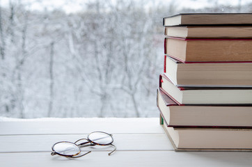 Old multi-colored books stand on a wooden shelf against the backdrop of the winter forest