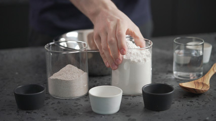 Fototapeta na wymiar man adds dry ingredients into flour in steel bowl on concrete countertop