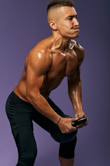 Fototapeta na wymiar hardworking shirtless man biting his lips doing a kettlebell workout, guy improving health at sport club. close up side view photo. isolated blue background, studio shot