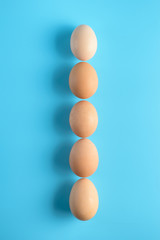 Five fresh brown chicken eggs in row on a blue background. Healthy good nutrition. Natural organic farm products.
