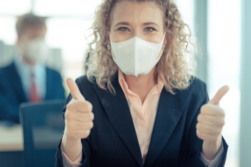 A business woman with curly blonde hair wearing a mask sitting in an office,  and looking at to camera, concept, contagion coronavirus