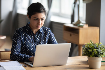 Focused Indian girl studying on laptop at home