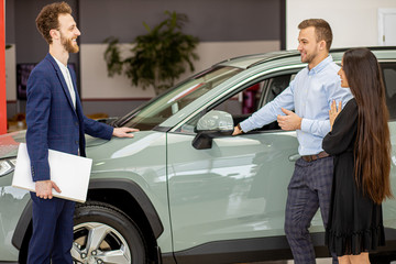 Fototapeta na wymiar young caucasian couple choosing new automobile with professional salesman in formal wear. nice positive salesman talking with clients