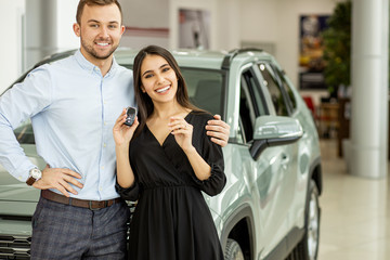 new owners of automobile, caucasian married couple posing in dealership, in car showroom. people, emotions concept. transport, vehicle concept