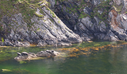 Donegal cliffs meet a tranquil sea with submerged rock.