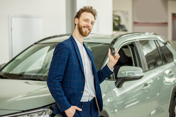 portrait of positive smiling happy man buyer in dealership, stand happily posing next to new car,...