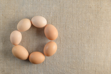 Seven fresh brown chicken eggs in shape of a circle on a canvas background. Healthy good nutrition. Natural organic farm products.