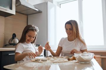 cheerful smiling woman and her daughter making cookies. close up photo. happiness. best time with mommy, positive atmosphere, mood at home