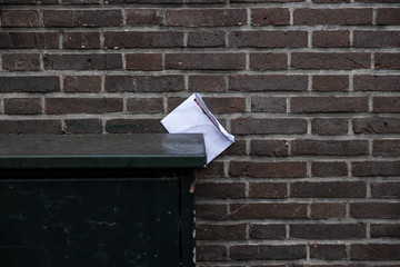 Gouda, South Holland/The Netherlands - February 15 2020: white open envelop jammed between a brick wall and a dark colored electrical box in the city center of Gouda