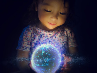 Small girl holds a glowing orb of modern technology.  Facing shot of the girl staring down into the bright ball in wonder.  Inspires ideas of creativity, awe, future, and destinations to come.