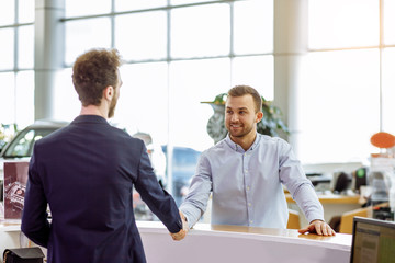 smiling customer man shake hand to pleasant consultant in formal wear. pleasant consultant welcomes...