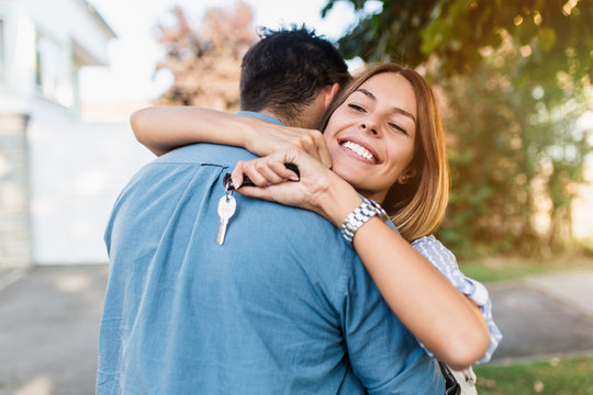 Beautiful happy young couple standing together outside in front of their new home.
