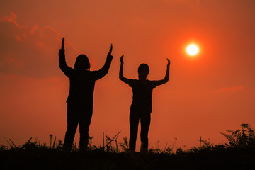 Silhouette of two teen girls praying to god with the bible.