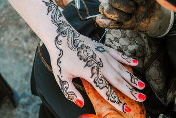 Woman applying a henna tattoo over a girl's hand