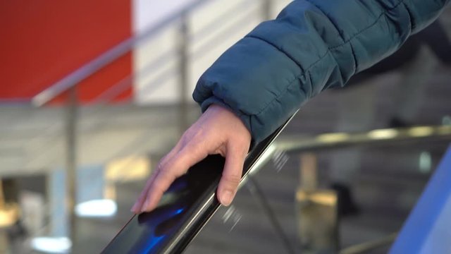A woman taps her finger on the railing of a glass escalator going down. Close-up of a woman's hand on the railing of a moving escalator in a shopping center. Faceless. Concept. 4K.