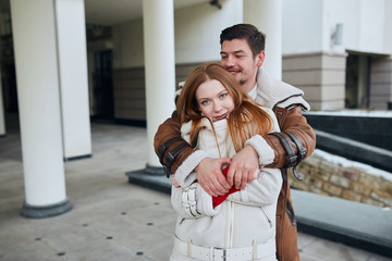 Two attractive cheerful young people hugging in the street. man standing behind her girlfriend, trying to get her warm. love, positive feeling and emotion. close up photo.