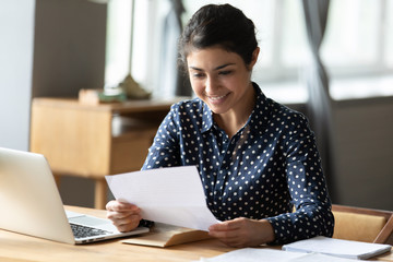 Smiling Indian woman read good news in paperwork correspondence