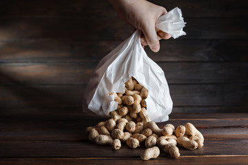 A torn paper bag in his hand that drops peanuts on a wooden table. The nuts in the shell crumbled....