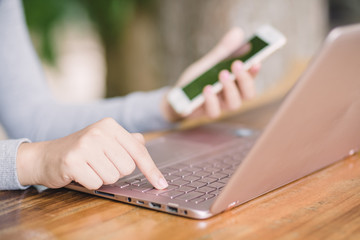 female holding smartphone getting message with confirmation making transaction on laptop computer