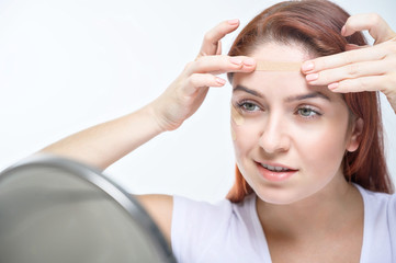 A woman sticks a kinezio tape on her forehead. Portrait of a girl makes applications on her face against facial wrinkles. An alternative to beauty injections at home.