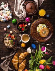 Fototapeta na wymiar Rustic easter breakfast flat lay with eggs bagels, tulips, croissants, egg, oatmeal with berries, colored quail eggs and spring holidays decorations. Top view.