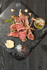 Raw lamb chops with salt, pepper and dry herbs on dark stone plate on black old rustic wooden table, flat lay 