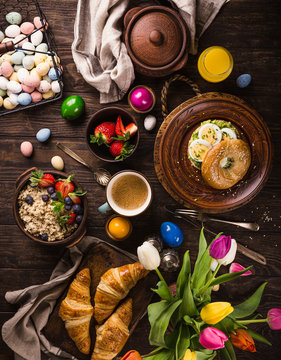 Rustic easter breakfast flat lay with eggs bagels, tulips, croissants, egg, oatmeal with berries, colored quail eggs and spring holidays decorations. Top view.