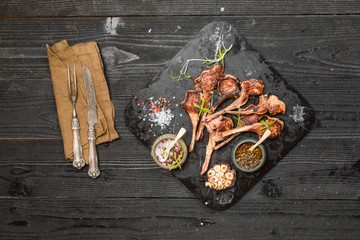 Grilling lamb chops with salt, pepper and dry herbs on dark stone plate on black old rustic wooden table, flat lay 