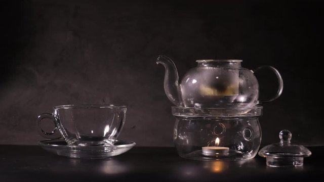 Pouring hot water to make green tea into teapot on kitchen. classic teapot made from glass and boil water by candle. hot drink and tea time concept