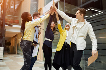 positive active young employees raising arms together, showing their unity, togetherness, one for...