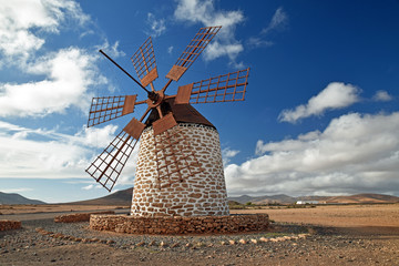 Traditional windmill at Tefia, Fuerteventura with wooden sails and roof, round whitewashed stone building. Blue sky and clouds.